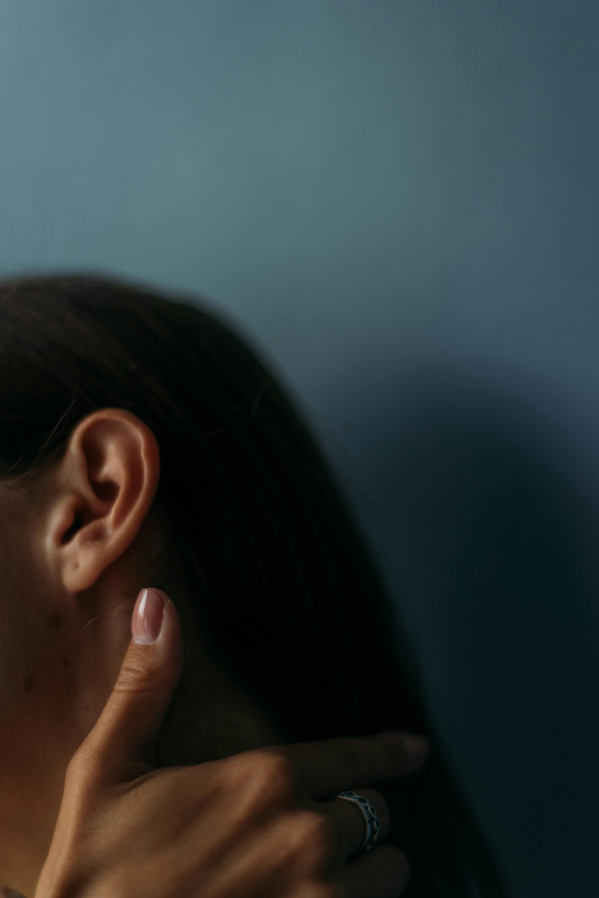 Detailed close-up of a woman's ear and hand against a moody backdrop, showcasing texture and elegance.